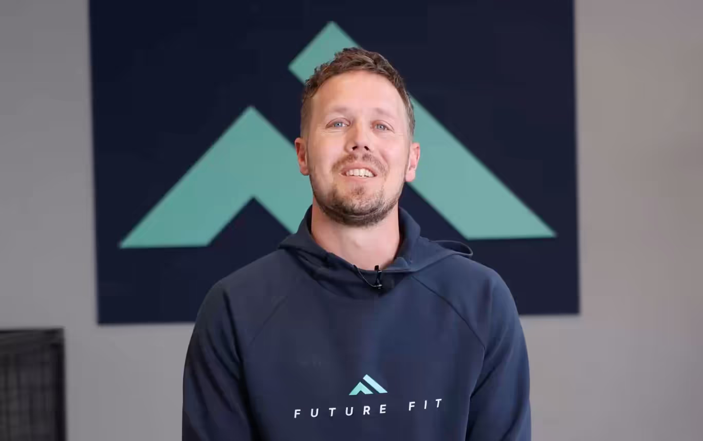 Hombre sonriente con sudadera de Future Fit sobre fondo azul y verde
