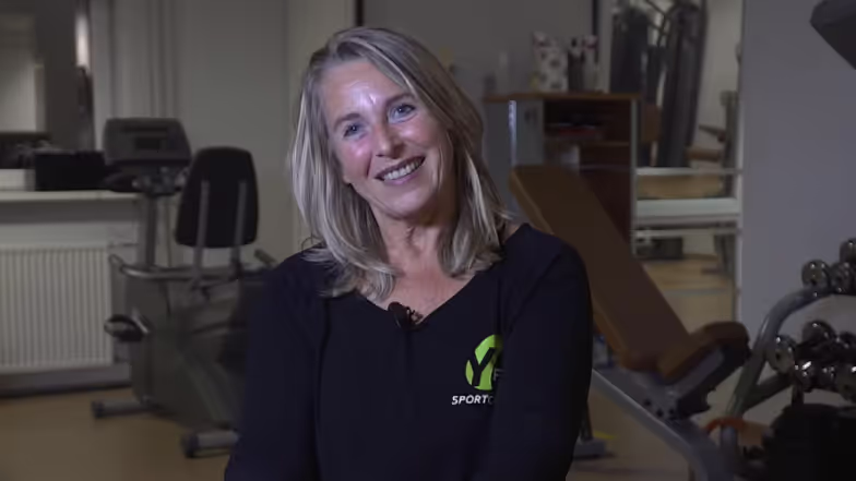 Mujer sonriente en una sala deportiva con equipamiento deportivo de fondo