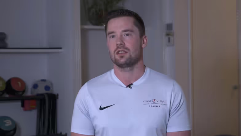 Entrenador con camiseta blanca de Nike en una sala de entrenamiento con equipamiento