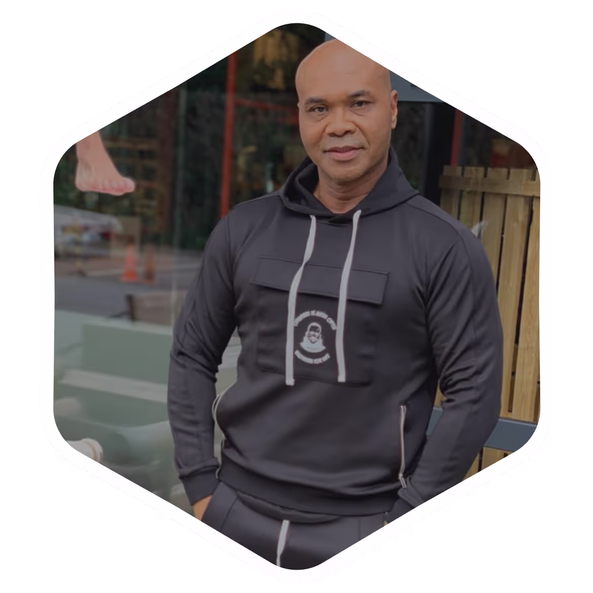 Older man in grey hoodie standing outside in front of wooden fence