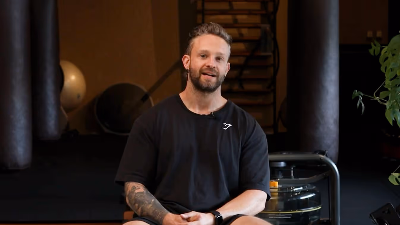 Hombre con camiseta negra sentado en sala de entrenamiento con máquinas de fitness