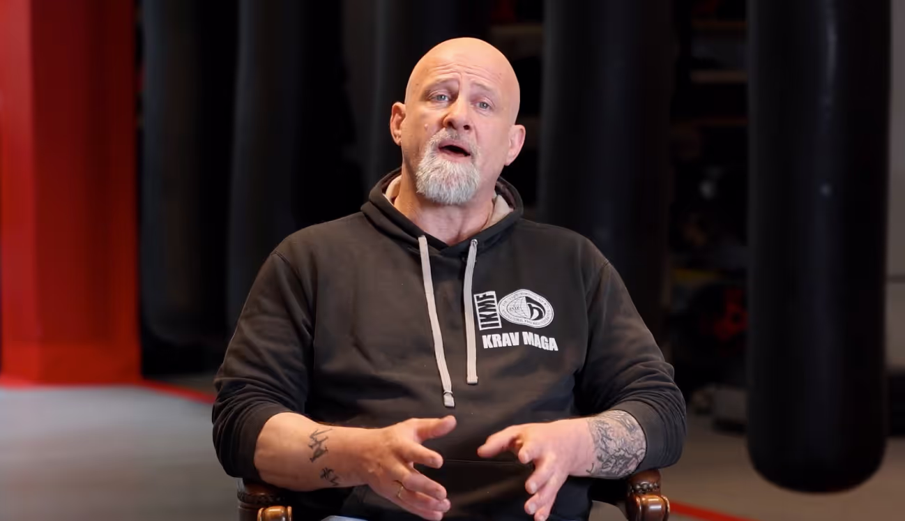 Hombre calvo con sudadera de Krav Maga explicando con gestos de manos