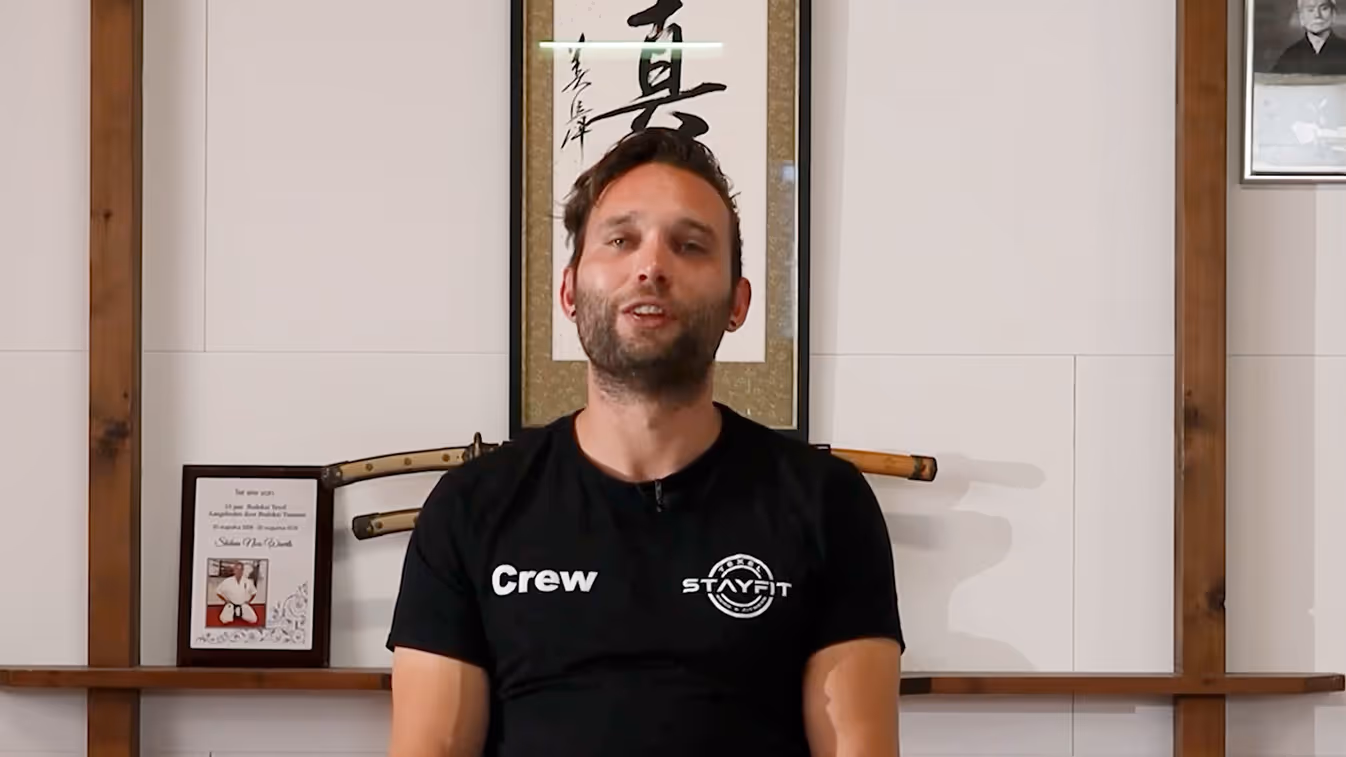 Persona con camiseta del equipo delante de caligrafía japonesa y armas de madera