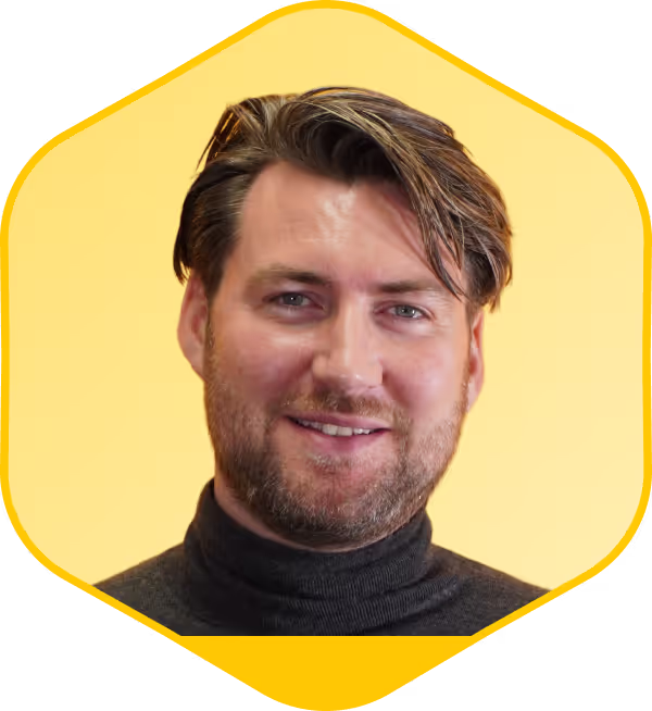 Hombre sonriente con pelo ondulado y jersey negro de cuello alto sobre fondo amarillo
