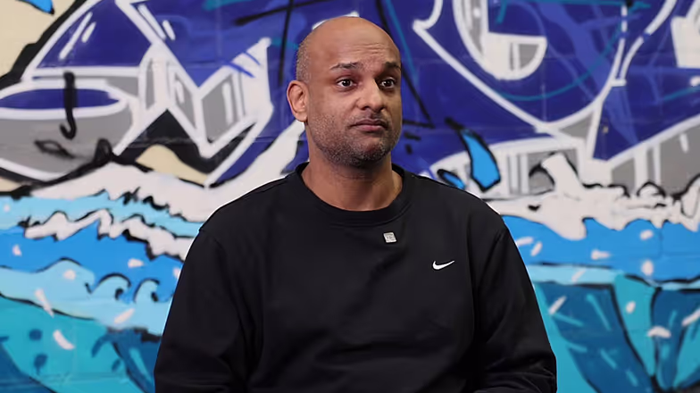 Hombre con camiseta Nike negra sobre fondo de grafiti azul y gris