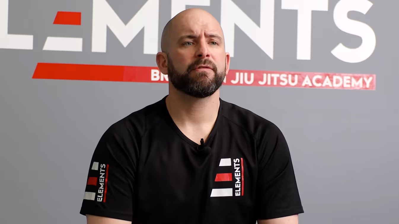 Hombre calvo con camiseta negra sobre fondo de Elements Jiu Jitsu Academy